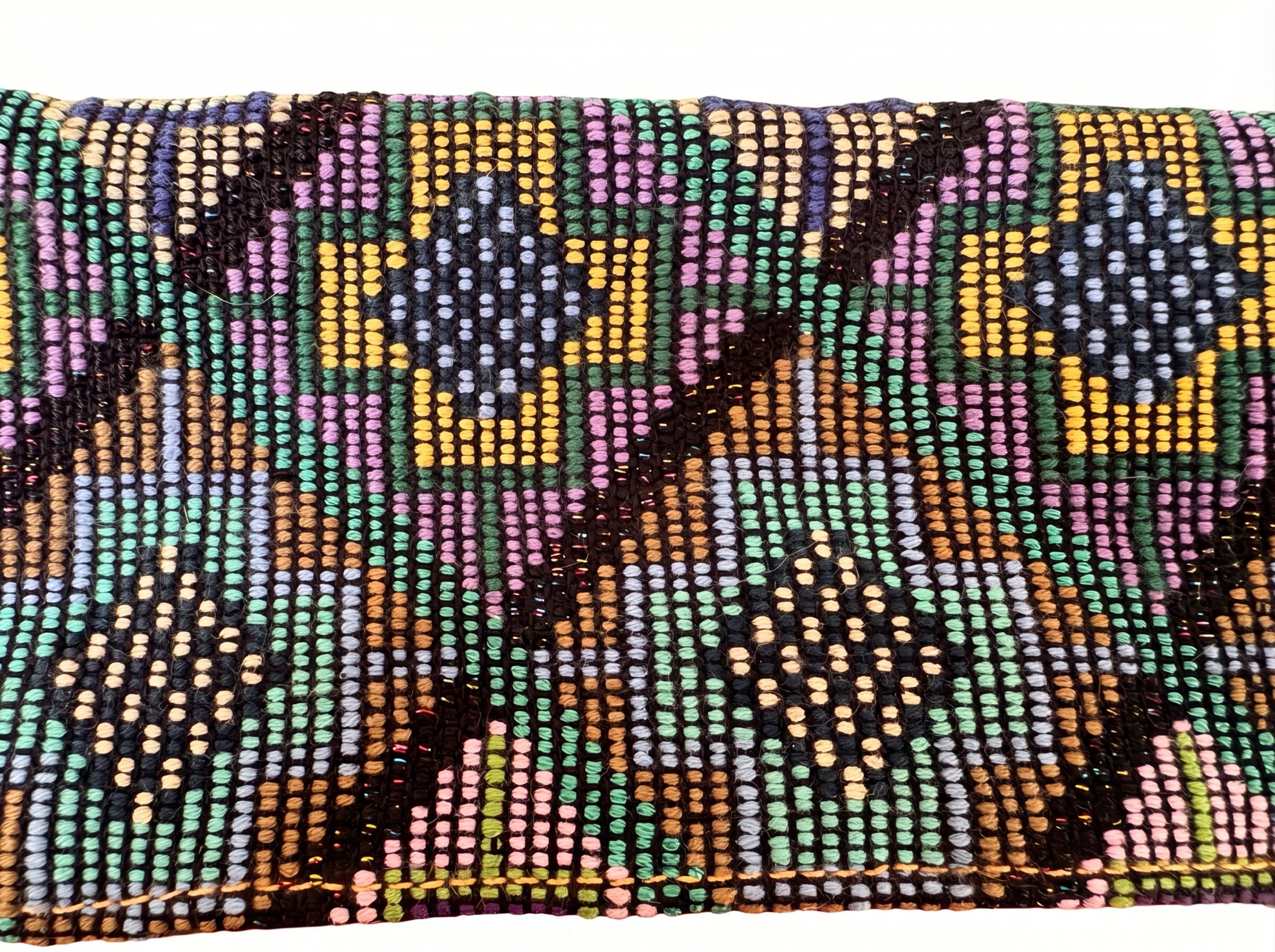TQC textile close-up showing cross and four-direction motifs woven in multicolor threads on a dark ground